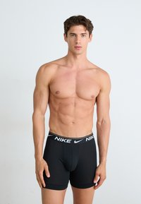 Schwarze Nike Boxershorts mit einem weißen Logo-Bund, enganliegendem Design und weichem Stoff, präsentiert von einem männlichen Model vor einem neutralen Hintergrund.
