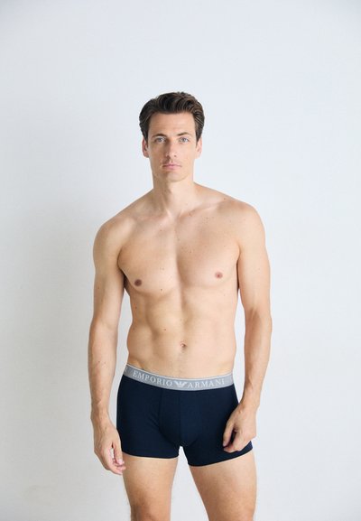Sötétkék Emporio Armani boxernadrág világosszürke derékrésszel, amelyen a márka logója ismétlődő mintában látható. Simára szőtt anyag.