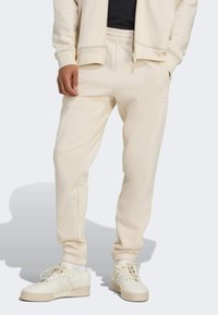 Pantalon de survêtement beige avec taille élastique, chevilles resserrées et poches latérales. Confectionné en matériau doux avec un détail de logo subtil près de la hanche droite.