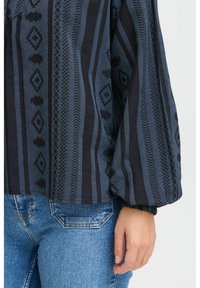 Blusa blu con motivo a righe verticali e design geometrici intricati, maniche lunghe a sbuffo e fondo orlato.