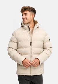 Veste rembourrée beige avec capuche, dotée d'une fermeture éclair et d'une doublure intérieure douce. Texture lisse avec des coutures visibles et une coupe décontractée.