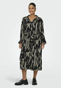 Robe rayée noire et crème avec un col, des manches longues et une ceinture à nouer. Présente une coupe ample et une longueur mi-jambe, assortie à des chaussures noires.