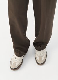 Hvite og grå joggesko med semsket og lær teksturer, med snøring og brune gummisåler, kombinert med brune bukser.