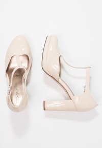 Beige blanka läder högklackade skor med rund tå, ankelrem och blockklack. Slät, glänsande yta med metalliska detaljer.