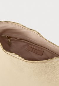 Εσωτερικό τσάντας από κρεμ δέρμα με ομαλή υφή, χρυστό φερμουάρ και ετικέτα που γράφει "Coccinelle Authentic Italian Leather".