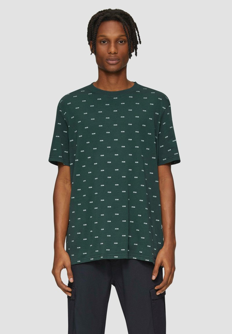 Groene t-shirt met korte mouwen en een wit herhalend tekstpatroon. Losse pasvorm, ronde halslijn, zacht materiaal en rechte zoom.