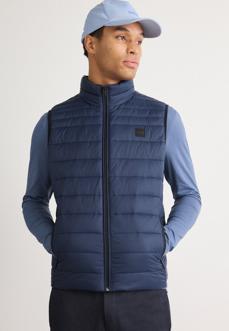 Tums fuscia krāsas izolēts veste ar vertikālu quilted struktūru, ar rāvējslēdzēja aizdari un sānu kabatām; uzvilkta virs gaiši zilas garām piedurknēm krekla.