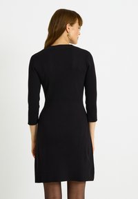 Robe noire côtelée avec manches trois-quarts, corsage ajusté et jupe légèrement évasée. Texture lisse, design minimaliste, couleur unie.