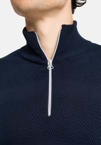 Marineblauer Reißverschluss-Pullover mit hohem Kragen, der strukturierte Strickmuster und einen silbernen Reißverschluss aufweist. Der Stoff ist weich und am Kragen gerippt.
