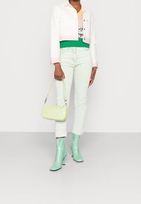 Veste en jean blanche cropped avec des rayures roses, pull en maille vert, jean vert clair, bottines menta brillantes et sac à main texturé vert clair.