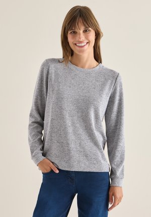 Grau, langärmliges Oberteil mit Rundhalsausschnitt, aus strukturiertem Stoff, kombiniert mit blauen Jeans. Das Oberteil hat eine lockere Passform und dezente Nähte.