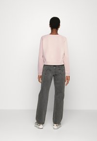 Felpa cropped rosa con maniche lunghe, abbinata a jeans grigi a vita alta e dal taglio morbido. Le scarpe presentano un design multicolore.