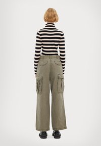 Tricou cu guler înalt, cu dungi negre și bej, prevăzut cu mâneci lungi, combinat cu pantaloni cargo largi de culoare verde măsliniu, detaliați cu buzunare cu clapetă și accente de text.