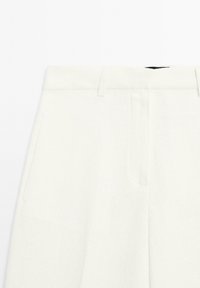 Weiße, maßgeschneiderte Hose aus strukturiertem Stoff mit flacher Vorderseite, seitlichen Taschen und einem sauberen Bunddesign.