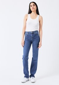 Vaqueros azules de cintura alta, pierna recta y cinco bolsillos. Combinados con una camiseta de tirantes blanca de canalé y zapatillas blancas.
