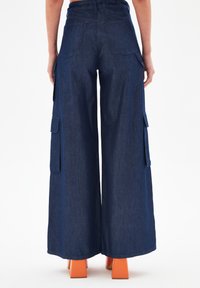 Wijde cargo-broek in donker denim, met zijzakken en een hoge taille. Gecombineerd met oranje blokhakken.