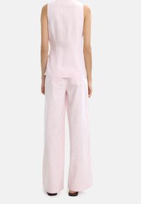 Jasnoróżowy bezrękawnik i pasujące spodnie o szerokich nogawkach. Miękka, teksturowana tkanina z haftowanymi tylnymi kieszeniami i luźnym krojem.