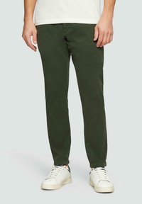 Dunkelgrüne Baumwollchinos, schmal geschnitten, mit Seitentaschen und einem schlichten Bund, kombiniert mit weißen Sneakers für einen lässigen Look.