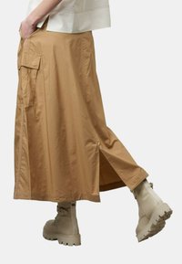 Gonna midi khaki con tasche cargo, spacchi laterali e tessuto leggero, abbinata a stivali beige con suola spessa per un look urbano.