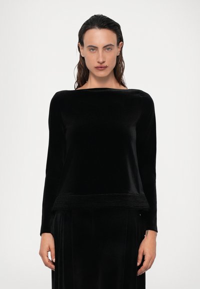 Top de terciopelo negro de manga larga con un escote amplio, que presenta un dobladillo inferior texturizado y un cuerpo liso. Líneas limpias y un ajuste relajado.