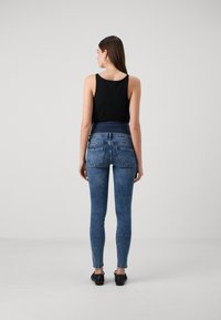 Top negro sin mangas combinado con jeans de denim azul ajustados. Los jeans presentan una cintura alta, bolsillos traseros estándar y un corte slim.