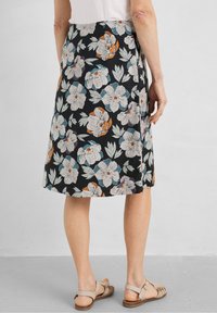 Woman wearing a black knee-length skirt with large white, blue, and orange floral prints, paired with beige sandals.