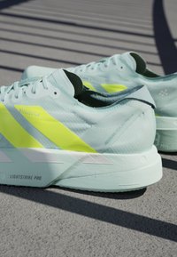 Jasnoniebieskie buty do biegania z neonowożółtymi paskami i białymi podeszwami oznaczone "LIGHTSTRIKE PRO", umieszczone na teksturowanej powierzchni z liniami cieni.