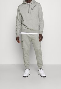 Grå sweatshirt med huva och framlomme, med en svart Nike-logga. Kombinerad med grå cargobyxor och vita sneakers.