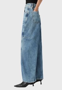 Heledad sinine denim laiad püksid kõrge vöökoht, suured küljetaskud ja tooriku lõpetamine, koos teravate mustade kontsadega kingadega.