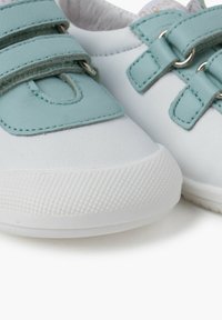Sneaker bianche con fasce in Velcro azzurro chiaro. Parte superiore in sintetico liscio, suola in gomma testurizzata e ritaglio circolare vicino ai lacci.