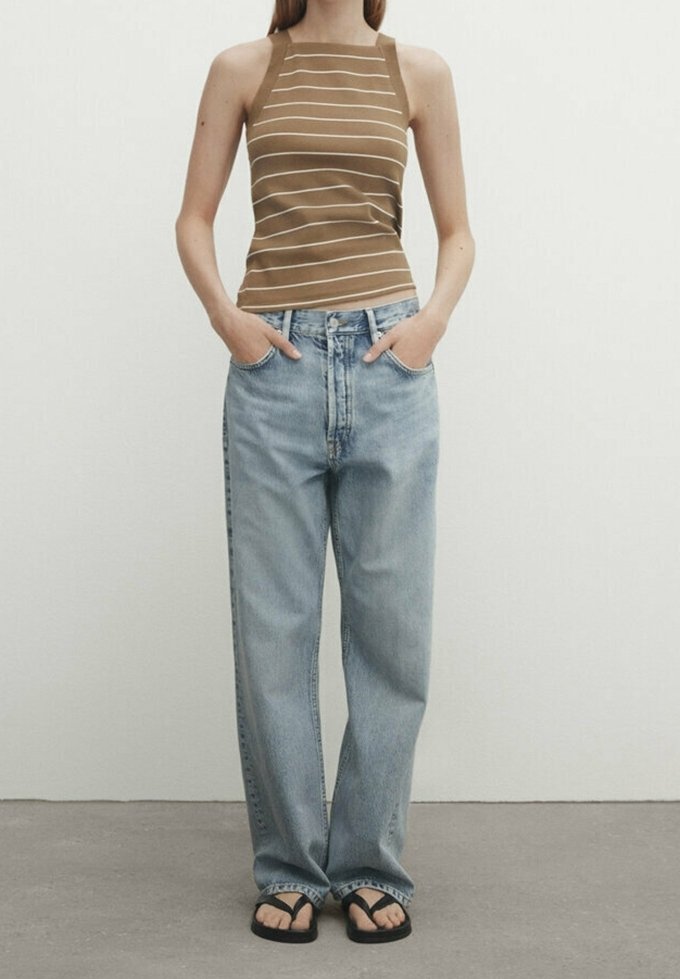 Débardeur marron à rayures associé à un jean taille haute bleu clair. Des tongs noires décontractées complètent la tenue.