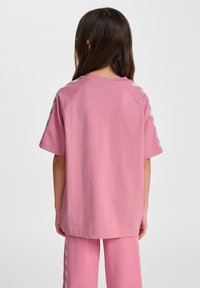 Lyserød bomulds T-shirt med kortærmer og løs pasform. Har hvide skrå striber på skuldrene. Glat tekstur, enkel design.