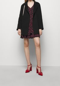 Zwarte oversized jas, bloemen roze jurk met ruches, en rode hoge hakken met bandjes en uitsparingen. Gladde texturen en gevarieerde ontwerpen.