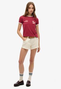 Rød kortærmet skjorte med hvid kant og logo detalje. Hvide shorts med fransk kant. Brun bælte. Bourgogne loafers. Stribede sokker.
