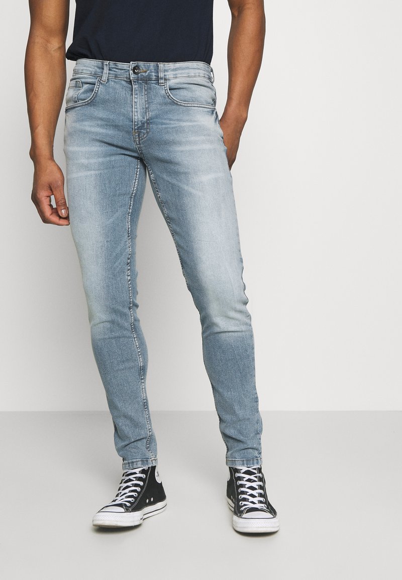 Lysblå slim-fit jeans med falmet tekstur, fem-lomme design, metal knaplukning og kontrasterende syninger. Sammen med sorte sneakers.
