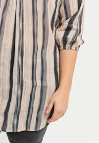 Blusa a righe in tessuto leggero con una combinazione di linee verticali rosa e nere. Presenta maniche a palloncino e una vestibilità morbida.