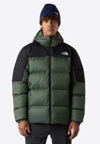 Puffjacka med grön kropp och svarta axlar, med huva, dragkedjestängning och elastiska muddar. Logotyp synlig på bröstet.