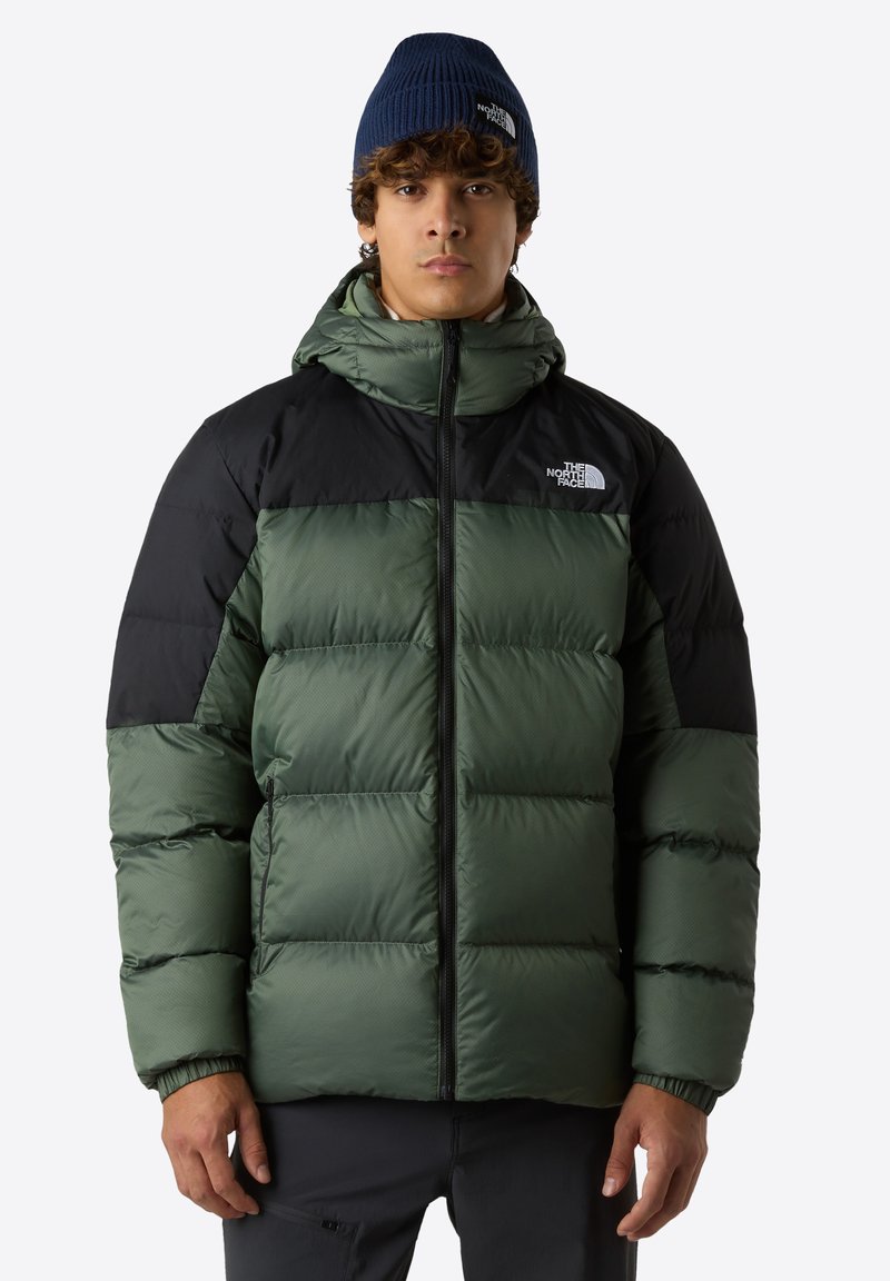 Puffjacka med grön kropp och svarta axlar, med huva, dragkedjestängning och elastiska muddar. Logotyp synlig på bröstet.