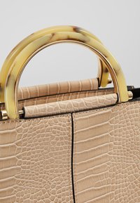 Sac à main beige à motif crocodile avec poignées arrondies en écaille de tortue jaune et métal doré sur fond neutre.