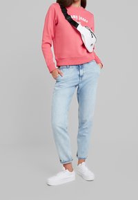 Rosa sweatshirt med vit text, ljusblå jeans och vita sneakers. En vit crossbody-väska bärs över axeln. Avslappnad outfit.