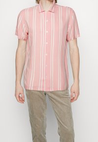Kortärmad skjorta med krage i ljusrosa med vita vertikala ränder, med knäppning framtill och en mjuk tygkänsla.