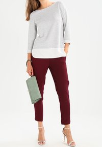 Gestreifter Langarm-Top in Grau und Weiß, kombiniert mit burgunderfarbener Slim-Fit-Hose. Hält eine hellgrüne Clutch und trägt silberne Riemchen-High-Heels.