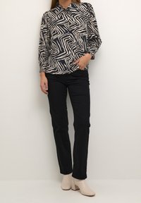 Blusa a maniche lunghe con un motivo zigzag nero e crema, abbinata a pantaloni neri e stivaletti beige. Tessuto morbido, vestibilità strutturata.