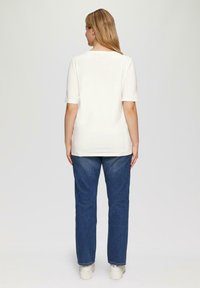 Witte t-shirt met korte mouwen en ronde hals, gecombineerd met donkerblauwe jeans. De stof lijkt glad en heeft een relaxte pasvorm.