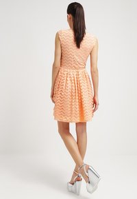 Robe couleur pêche avec un motif en zigzag, manches courtes et taille élastique. Associée à des sandales à plateforme argentées.