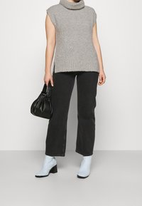 Pull sans manches gris à col bénitier, jean noir droit, bottines à talons bleu clair et sac à main noir plissé.