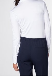 Camicia bianca a maniche lunghe con una texture liscia e polsini abbottonati, abbinata a pantaloni blu con vita elasticizzata e tasca posteriore.