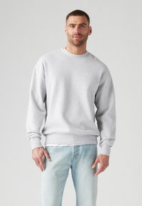 Gray sweatshirt made of cotton blend, featuring a round neckline, ribbed cuffs and hem, and a minimal logo on the chest. Model wears light jeans.