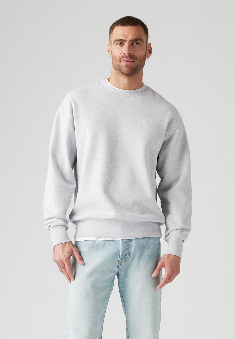 Gray sweatshirt made of cotton blend, featuring a round neckline, ribbed cuffs and hem, and a minimal logo on the chest. Model wears light jeans.