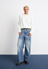 Sudadera blanca de gran tamaño con un pequeño logo, pantalones vaqueros de pierna ancha en azul y zapatos de plataforma negros. Diseño simple con un corte relajado.